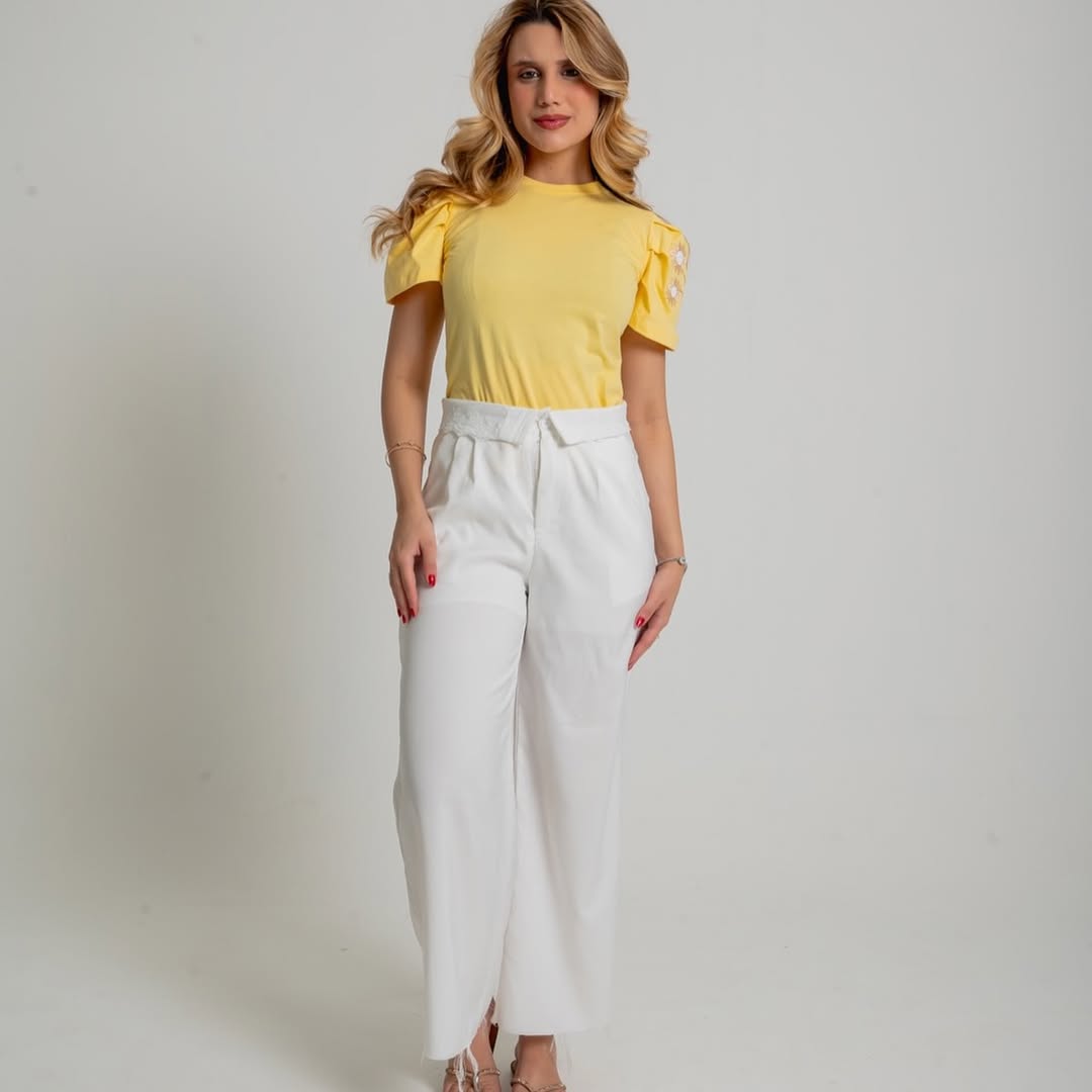 Modelo com T-shirt amarela de manga bordada com margaridas e calça branca da Venâncio Modas