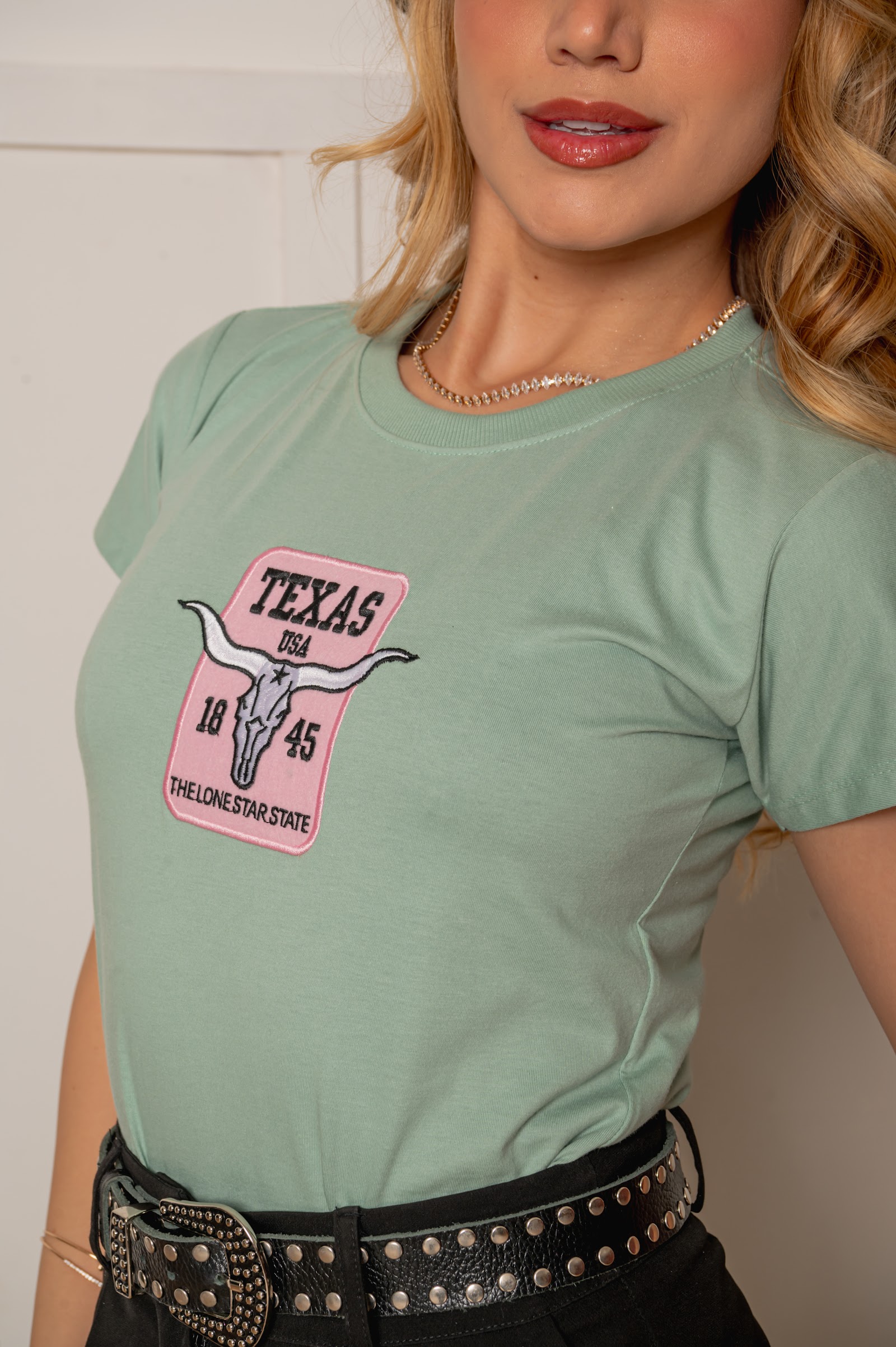 Detalhe do bordado Texas em tons de rosa na T-shirt verde
